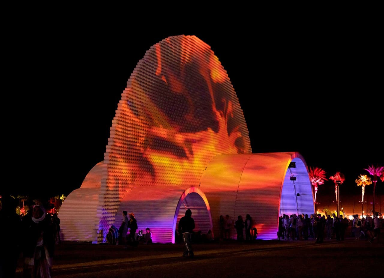 Circular Dimensions × Microscape — a five-story dome of PVC tubing glowing in fiery orange and magenta against the night sky, a crowd gathered beneath it at the Coachella festival.