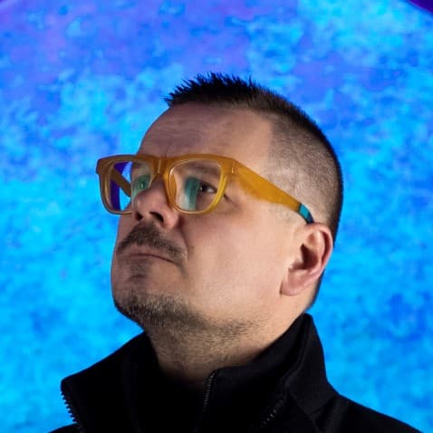 Portrait of Cristopher Cichocki, in profile before a vivid blue-and-violet projection.